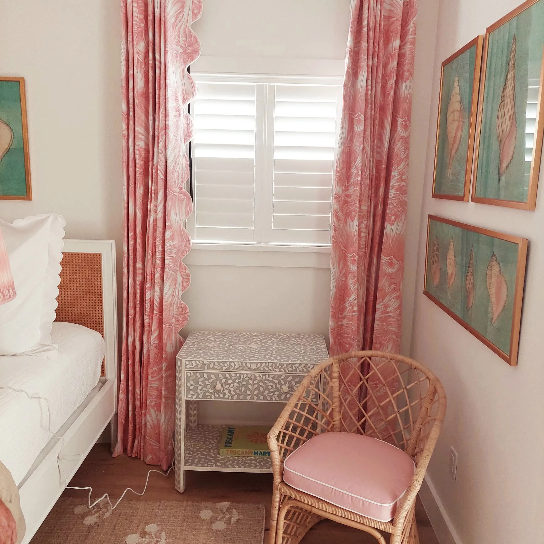 Plantation shutters with pink drapery and a woven chair